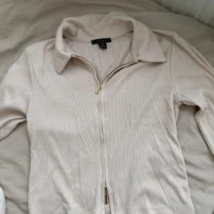 Beige ribbad kofta med dragkedja  - Säljer en beige ribbad kofta med dragkedja framtill och klassisk krage. Tröjan har långa ärmar och är perfekt för lager-på-lager. Enkel och stilren design som passar till mycket. Strl M men passar för mig med xs/s