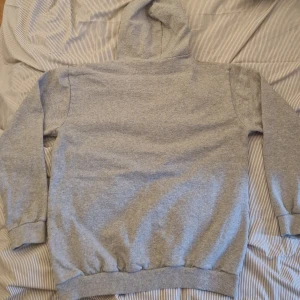 Grå hoodie från FILA - Säljer en klassisk grå hoodie från FILA med stor logga framtill. Tröjan har huva med dragsko och en stor magficka. Perfekt för en avslappnad stil och enkel att matcha med det mesta.