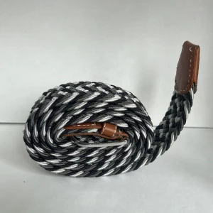 flätat bälte - Snyggt flätat bälte i svart, grått och vitt med bruna läderdetaljer och silverfärgat spänne. Perfekt accessoar för att lyfta din outfit med en modern touch. Bältet har ett klassiskt spänne och passar till många olika stilar.