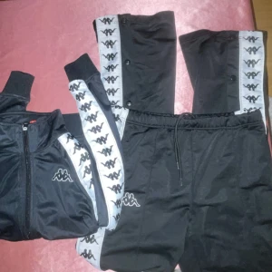 Svarta träningsbyxor från Kappa med logga - Svarta träningsbyxor från Kappa. Byxorna har resår och snörning i midjan samt tryckknappar längs sidorna. För att köpa endast byxorna 200kr. Både tröja och byxa 500kr