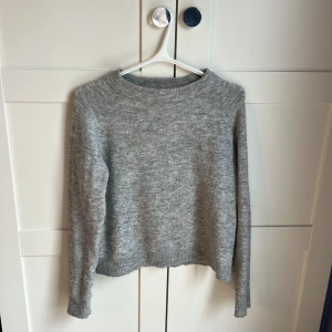 Grå stickad tröja från Vero Moda - Mysig grå stickad tröja från Vero Moda med rund halsringning och ribbade muddar. Perfekt för lager-på-lager och enkel att matcha med jeans eller kjol. Klassisk modell med lång ärm och mjukt material.