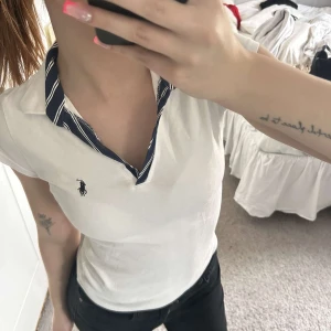 Vit piké från Polo Ralph Lauren med randig krage - Vit pikétröja från Polo Ralph Lauren med klassisk blåvit randig krage och broderad logga på bröstet. korta ärmar och figurnära passform. Superfin till vardagliga tillfällen! Visar inte mycket tecken på användning 