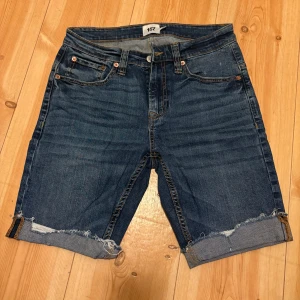 Blå jeansshorts från 157 - Säljer ett par klassiska blå jeansshorts från 157 med upprullade och fransade benslut. Shortsen har fem fickor, knappgylf och normal passform. Perfekta för sommaren!