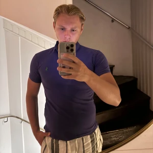 Lila slim fit piké från Polo Ralph Lauren - Säljer en lila slim fit piké från Polo Ralph Lauren med klassisk krage och korta ärmar. T-shirten har en liten grön logga broderad på bröstet och är tillverkad i mjuk bomull som sitter snyggt mot kroppen.