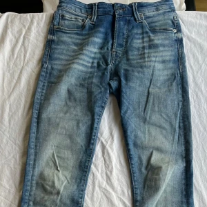 Jack & Jones Glenn Super Stretch Jeans - Snygga blå jeans från Jack & Jones, modell slim Glenn med superstretch för extra komfort. Slim fit med klassisk femficksdesign och ljus tvättade detaljer. Perfekt passform och stilren look. Ena sömen på bakfickan har lagats (bild 5) men syns knappt. Storlek W28L32. Förutom den lilla lagningen är i i fint skick och rena.