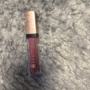 Matt flytande läppstift CC - Snyggt matt flytande läppstift från CC med roséguldfärgat lock och transparent hylsa. Färgen är en djup, kall rosa med lila underton som ger en trendig look. Perfekt för dig som gillar att ha markerade läppar med en modern finish.