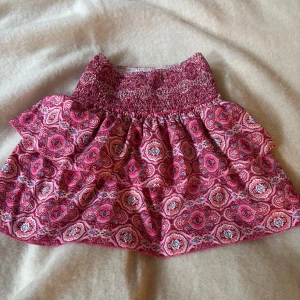 Rosa mönstrad kortkjol med volang - Supersöt kortkjol i rosa med paisley-inspirerat mönster och bred smock i midjan. Kjolen har även inbyggda shorts i vitt tyg som syns på andra bilden!💗Köpta från vinted, finns ingen lapp med storlek men skulle säga M.