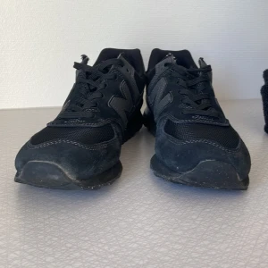Svarta New Balance sneakers - Säljer ett par svarta New Balance sneakers med klassisk N-logga på sidan. Skorna har en snygg mix av mocka och mesh, platt sula och snörning. Perfekt för dig som gillar stilrena och sportiga skor med skön passform.