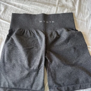 Mörkgrå träningsshorts från NVGTN - Snygga mörkgrå träningsshorts från NVGTN med hög midja och stretchigt material som sitter skönt. Perfekta för gymmet eller löprundan, med en clean look och diskret logga framtill i vitt. Passformen är tight och materialet känns mjukt mot huden.