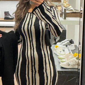 Randig långklänning i svart och beige - Säljer en snygg långklänning med vertikala svarta och beige ränder. Klänningen har en tight passform som framhäver figuren och är ärmlös. Perfekt för dig som gillar en stilren och modern look.