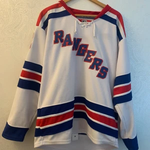 New York Rangers Carl Hagelin hockeytröja - Säljer en officiell NHL New York Rangers tröja med Hagelin #62 på ryggen. Tröjan är vit med blå och röda ränder, har lång ärm och snörning vid halsen. Märkt med Reebok och CCM, tillverkad i Kanada. Perfekt för dig som vill sticka ut på match eller i stan. Eller för dig som vill ha en episk hockeytröja i din garderob!