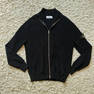 Svart kofta från Stone Island - Svart ribbstickad kofta från Stone Island med hel dragkedja framtill och klassisk logotyp-patch på vänster ärm. Tröjan har långärmad passform och står ut med sin stilrena look och mjuka stickade material. Perfekt för dig som gillar streetwear och snygga detaljer. Helt perfekt för alla säsonger och runt om året. Den är helt ny och oanvänd och originella tags medföljer vid köp. Passar lite slim på armarna vilken är perfekt ifall man gymmar och vill visa sin progress 🙏
