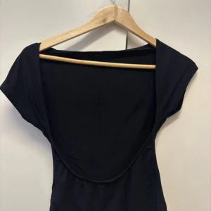 Svart topp med öppen rygg - Svart topp med snyggt djup öppen rygg. Tunn och mjuk bomullskänsla, figurnära passform och korta ärmar. Perfekt för dig som gillar minimalistisk stil med en twist. Enkel att matcha med jeans eller kjol. 