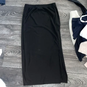 Svart långkjol med slits från SHEIN - Svart långkjol från SHEIN med en clean och enkel look. Kjolen har en snygg slits på sidan som ger extra edge och är tillverkad i ett stretchigt material som sitter skönt. Perfekt för dig som gillar minimalistisk stil.