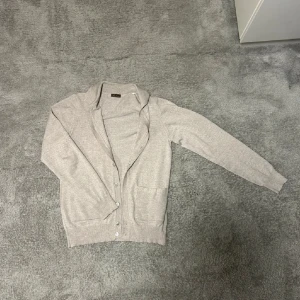 Beige kofta från Stenströms - Snygg beige kofta från Stenströms i mjuk stickad bomull. Klassisk design med långa ärmar, ribbade muddar och knappar framtill. Perfekt att slänga över en t-shirt eller ha som lager. Två praktiska fickor framtill för mobilen eller nycklar.