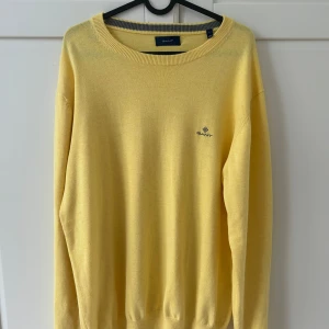 Gul stickad tröja från GANT - Fräsch gul stickad tröja från GANT i storlek L. Tröjan har rund halsringning med ribbad kant och diskret GANT-logga broderad på bröstet. Mjuk och lätt kvalitet som passar perfekt till vår och sommar. Långa ärmar och klassisk passform.