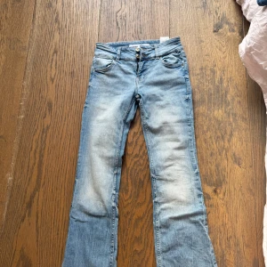Bootcut jeans från Bershka ljusblå - Snygga ljusblå bootcut jeans från Bershka med klassisk femficksdesign och dubbla knappar i midjan. Jeansen har en lätt tvättad look och är tillverkade i mjukt denimtyg som sitter skönt. Perfekt för dig som gillar retrovibbar och vill ha en cool siluett.