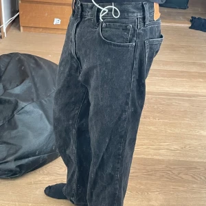 Levi's 551 svarta wide jeans W30 L32 - Säljer ett par svarta Levi's 551 jeans med bred passform och klassisk femficksdesign. Jeansen har en cool tvättad look och är tillverkade i robust denim. Perfekt för dig som gillar avslappnad stil och vill ha ett par jeans med lite extra utrymme i benen. Köpte för 1000 och säljer för 500 ni kännar bra på det och dom är kanpt använd 