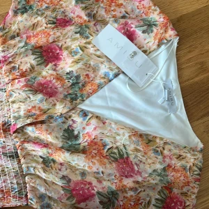 Blommig långklänning från Amisu - Säljer en superfin långklänning från Amisu med blommigt mönster i rosa, orange, grönt och blått på ljus botten. Klänningen har korta ärmar, smock i midjan och volang nedtill. Perfekt för sommarens alla tillfällen!