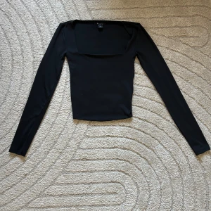 Svart långärmad topp med fyrkantig ringning - Supersnygg svart topp med lång ärm och fyrkantig ringning som framhäver halsen på ett elegant sätt. Enkel men trendig design som passar både till vardags, fest eller att matcha med jeans/kjol. Toppen är i fint skick och används inte längre, därför säljer jag den vidare.