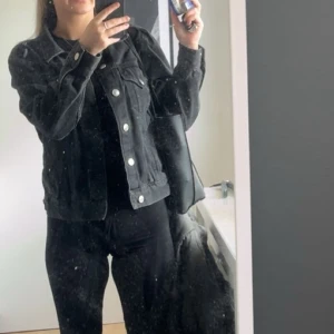 Svart jeansjacka med knappar - Snygg svart jeansjacka med klassisk passform och silvriga knappar framtill. Jackan har två bröstfickor med lock och knappar, samt en cool, tidlös look som funkar till många stilar. Perfekt för dig som gillar street och casual.