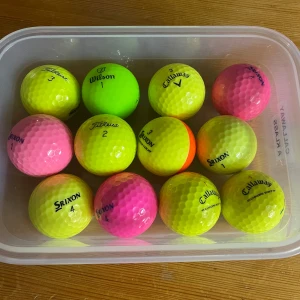 Färgglada golfbollar i toppskick – 12 st blandade märken - Säljer en låda med 12 stycken färgglada golfbollar av hög kvalitet. Märken som Titleist, Callaway, Wilson och Srixon. Alla i mycket fint skick och redo för spel – perfekt för dig som vill synas på banan och lätt hitta bollarna i gräset. Lådan på bilden ingår.