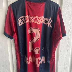 Barça x Cactus Jack fotbollströja - Snygg FC Barcelona fotbollströja i samarbete med Cactus Jack. Tröjan har breda vertikala ränder i mörkblått och rött, med klubbmärke och Nike-logga på bröstet. Tryck med nummer 2 och Cactus Jack på ryggen. Tillverkad i lätt polyester med korta ärmar och krage.