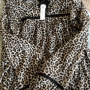 Leopardmönstrad blus  från Lindex - Snygg leopardmönstrad blus från Lindex med svarta spetsdetaljer och knappar vid halsen. Blusen har långa ärmar och ett lätt rynkat tyg som ger en cool och trendig look. Hör av dig vid frågor💕