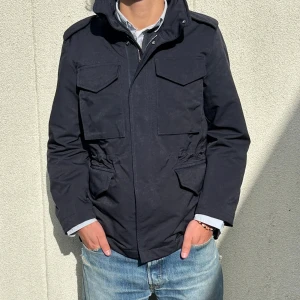 Mörkblå fieldjacket från Arket i nyskick - Snygg mörkblå fieldjacket med fyra stora fickor framtill och hög krage. Jackan har dragkedja och tryckknappar. Perfekt för dig som vill ha en stilren och funktionell jacka med lite militärvibbar. Hör av er vid frågor!👍