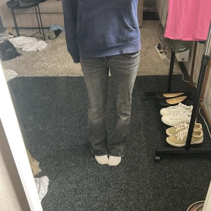 Svarta low waist bootcut jeans från gina tricot - Säljer ett par svarta Replay jeans med bootcut passform och låg midja. Jeansen har snygga detaljer som fickor med lock och knappar bak, samt slitningar för en cool look. Materialet är klassisk jeans med stretch för skön passform.