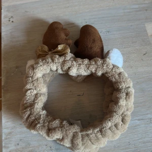 Diadem med renhorn och rosett - Supergulligt fluffigt diadem i beige plysch med mjuka bruna renhorn, vit detalj och en glittrig guldrosett. Perfekt accessoar för att sticka ut och ge en lekfull touch till din look.