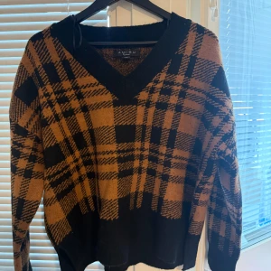 Rutig brun och svart stickad tröja NewYorker  - Säljer en oversized stickad tröja från NewYorker i brunt och svart med rutig design. Tröjan har v-ringning och långa ärmar. Storlek M