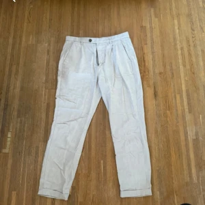 Linnebyxor beige  - Snygga ljusbeige linnebyxor från Visual Clothing Project. Byxorna har klassisk passform med pressveck, sidfickor och uppvikta benslut. Perfekta för en chill och stilren look under varmare dagar.