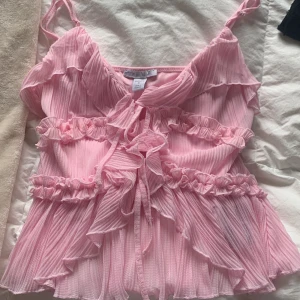 Rosa volangtop från Amisu - Supersöt rosa linnetopp från Amisu med tunna axelband, volanger och knyt fram.  Oanvänd 