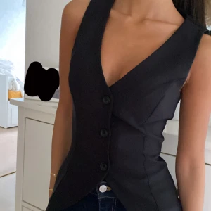 Svart figursydd väst med knappar - Snygg svart väst med djup v-ringning och tre stora knappar framtill. Figursydd modell från Ginatricot, köpt för 459, enbart använd en gång och i väldigt bra skick!🩷