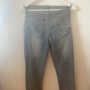 Blå/grå jeans med stjärndetaljer - Snygga grå/ljusblåjeans med raka ben(lite bredare under knäna) och mid waist midja. På ena bakfickan finns en cool stjärna i denim och framtill är tre guldiga stjärnor broderade. Jeansen har klassisk femficksdesign och är perfekta för dig som vill sticka ut lite extra.