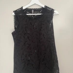 Svart spetsblus från Culture - Supersnygg svart blus från Culture i genombruten spets med blommigt mönster. Ärmlös modell med rund hals och fina spetsdetaljer längs kanterna. Perfekt för dig som vill ha en elegant och trendig look.