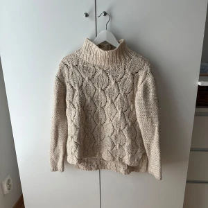 Beige stickad polotröja från H&M - Säljer en chunky beige stickad polotröja från H&M i storlek XS. Tröjan har ett snyggt strukturmönster framtill och bak, hög polokrage och långa ärmar. Perfekt för kalla dagar när du vill vara både varm och stilren.