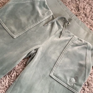 Mintgröna velourbyxor Juicy Couture - Supermjuka mintgröna velourbyxor från Juicy Couture med bred resår i midjan och snörning. Stora fickor fram och bak med knappar, samt broderad logga på ena benet. Byxorna har en bootcut passform och ger en chill men ändå snygg vibe. Små defekter på 3 ställen, kan skicka bild på det om någon är intresserad. Midjemått 34 och innerben 82❤️