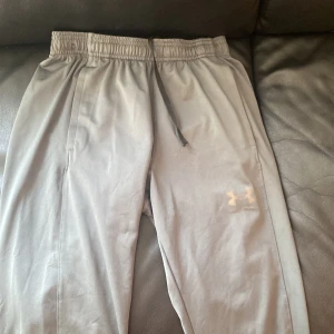 Grå mjukisbyxor från Under Armour m - Snygga  mörk olivgrön mjukisbyxor från Under Armour med elastisk midja och snörning. Byxorna har raka ben, sidofickor och en diskret logga på låret. Perfekta för chill eller träning, tillverkade i mjukt och lätt syntetmaterial.