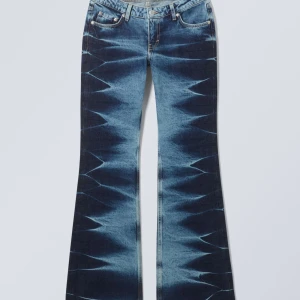 Blå bootcut jeans med mönster - Säljer ett par blå bootcut jeans med unikt, nästan zigzag-liknande mönster längs benen. Jeansen har låg midja och klassisk femficksdesign. Materialet är jeans och färgtonen är mörkblå med ljusare detaljer. Perfekta för dig som vill sticka ut med din stil.