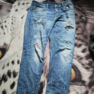 Dsquared2 Twinphony blå jeans - Snygga blå Dsquared2 Twinphony jeans med slitningar, hål och färgstänk för en riktigt edgy look. Klassisk femficksmodell med raka ben och coola detaljer. Perfekta för dig som gillar streetstyle och vill sticka ut.