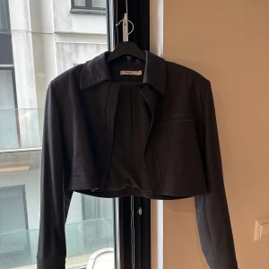 Mörkgrå croppad kavaj från NA-KD OVERSIZED - Snygg mörkgrå croppad kavaj från NA-KD med klassisk krage och långa ärmar. Jackan har en stilren design med diskreta sömdetaljer och är perfekt för dig som gillar en trendig och clean look. Passar till allt från jeans till kjol.
