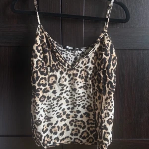 Leopardmönstrad topp y2k - Snygg linnetopp med leopardmönster i beige, brunt och svart. Tunt material och smala axelband, perfekt för en trendig look. V-ringad framtill och lätt croppad passform.