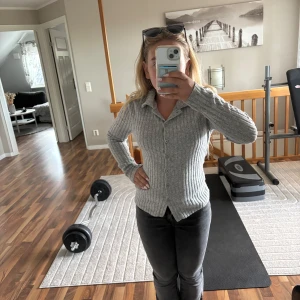 Grå ribbad kofta från SHEIN - Grå ribbad kofta från SHEIN i storlek S. Tröjan har lång ärm, knappar framtill och är tillverkad i mjuk polyesterblandning. Snygg och enkel modell som passar perfekt till jeans eller kjol.