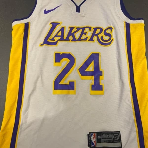 Lakers Bryant 24 basketlinne Nike storlek small - Säljer ett ikoniskt Los Angeles Lakers basketlinne med nummer 24 och Bryant på ryggen. Linnet är vitt med gula och lila detaljer, tillverkat i lätt polyester som andas. Perfekt för dig som älskar basket och vill hylla Kobe Bryant.