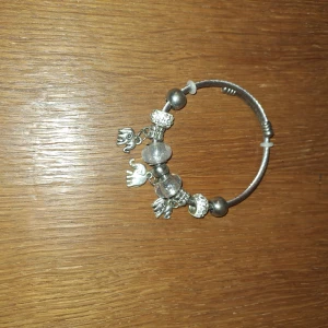 Silverfärgat armband med elefanthängen - Coolt armband i silverfärg med flera elefanthängen och glaspärlor. Armbandet har en stilren metalltråd som bas och detaljerade pärlor i både metall och glas. Perfekt accessoar för dig som gillar unika smycken med djurmotiv.