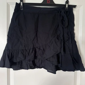 Marinblå omlottkjol från NLY Trend - Marinblå kort omlottkjol från NLY Trend i luftig linnemix. Kjolen har volangkant nedtill och knytband i midjan för en snygg och avslappnad look. Perfekt för varma dagar när du vill känna dig både bekväm och trendig.