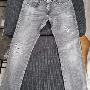 Replay Anbass grå jeans med slitningar 33,32 - Säljer ett par Replay Anbass jeans i grå tvätt med snygga slitningar och distressed detaljer. Klassisk femficksmodell med raka ben och coola bakfickor. Perfekta för dig som gillar en avslappnad men trendig look.