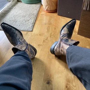 Ormskinnsmönstrade cowboy boots MAN - Säljer ett par sjukt snygga cowboy boots från MAN i storlek 44, jag har strlk 42,5 och dom passar mig bra med extra sula.                  Skorna har ett ormskinnsmönster i bruna och svarta toner, spetsig tå och låg klack. Tillverkade i skinn med Goodyear-typ sula. Perfekta för dig som vill sticka ut med din stil. Finns i Umeå om man vill prova! Peace